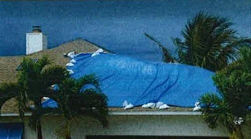 A damaged roof covered with a blue tarp